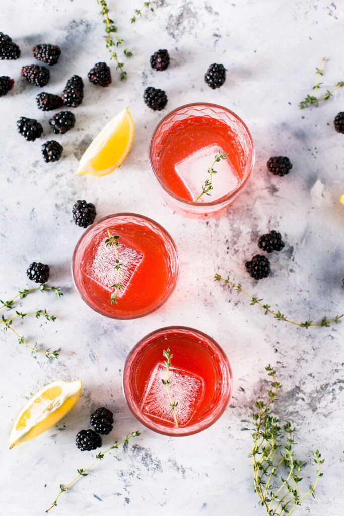 Refreshing From Scratch Blackberry Lemonade garnished with thyme lemon wedges and blackberries
