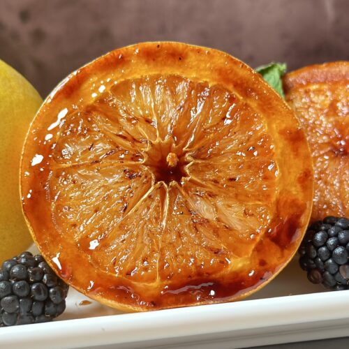 grilled grapefruit sliced in two halves brûlée on a white platter garnished with blackberries