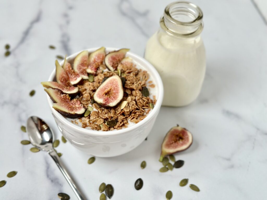 Vanilla Kefir and Cinnamon Pepita Granola Bowl Picture on Counter with spoon and figs kefir in a glass jar