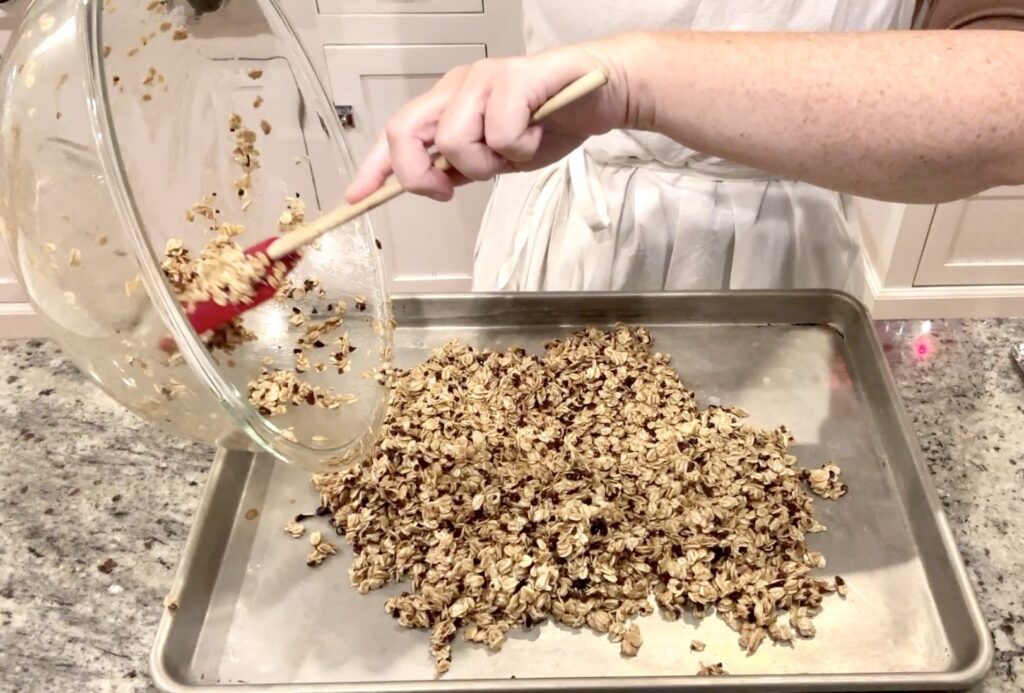 woman pouring mixed granola ingredients onto a half sheet pan