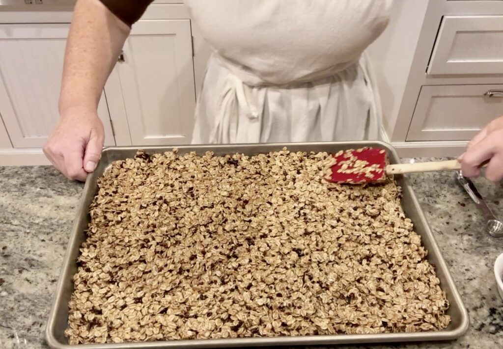 women spreads granola out in half sheet pan with Williams Sonoma red spatula and flatens granola out evenly