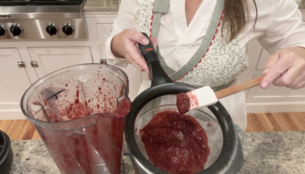 woman making blackberry purre in a Vitamix blender and straining it through a mesh strainer