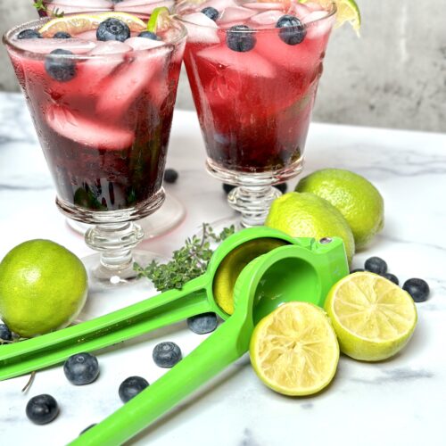 non alcoholic mocktail blueberry lime spritzer on marble counter with a green lime squeezer
