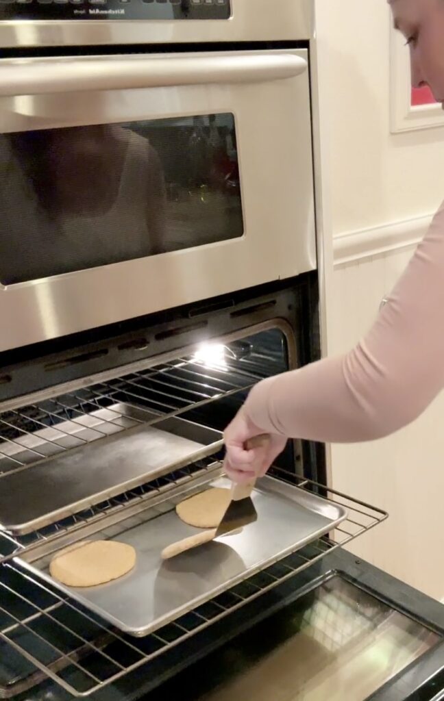 woman in a pink shirt placing third whole wheat einkorn pita on a hot preheated half baking sheet pan
