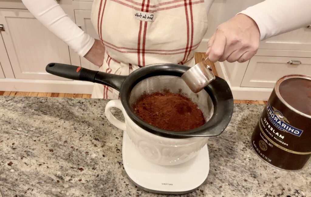 woman in apron is sifting cocoa powder