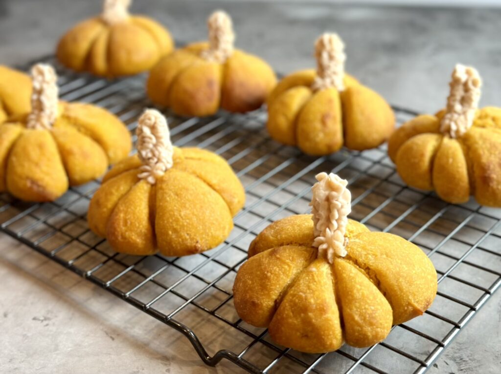 Picture of festive Einkorn sourdough pumpkin dinner rolls on a wire rack with honey cinnamon butter, stems.