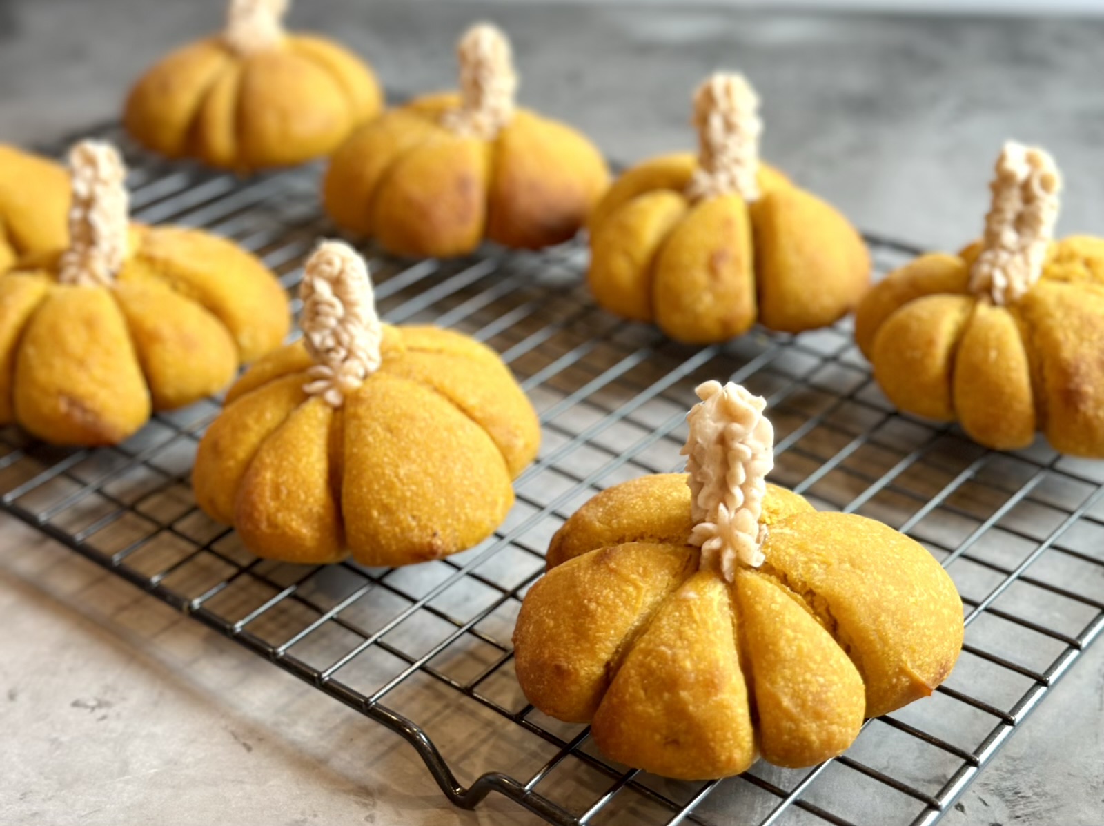 Picture of festive Einkorn sourdough pumpkin dinner rolls on a wire rack with honey cinnamon butter, stems.