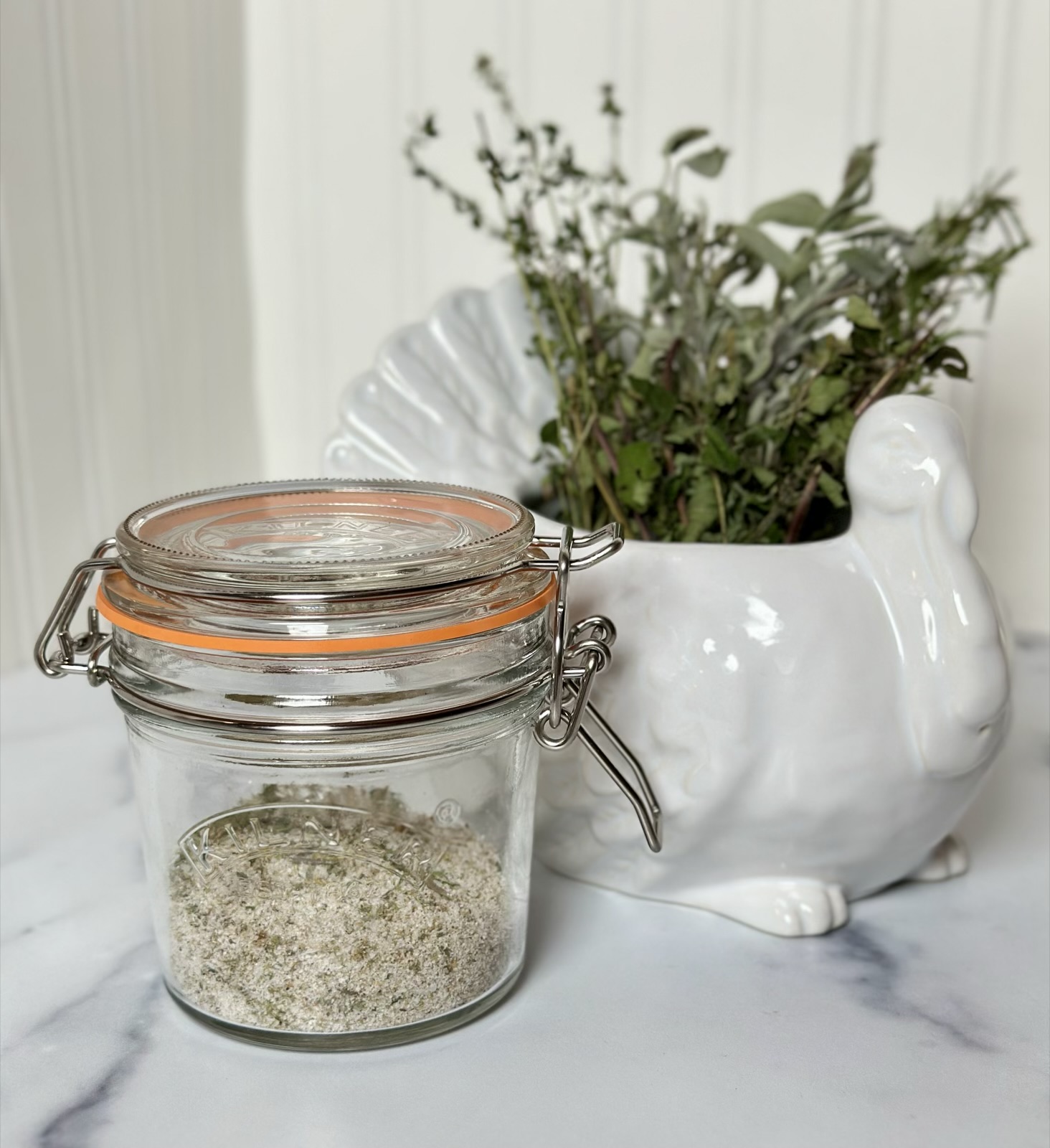 Picture of Homemade Citrus Herb Dry Brine for Turkey, steak and chicken displayed in a Kilner jar with a pottery barn white porcelain turkey gravy boat filled with fresh herbs