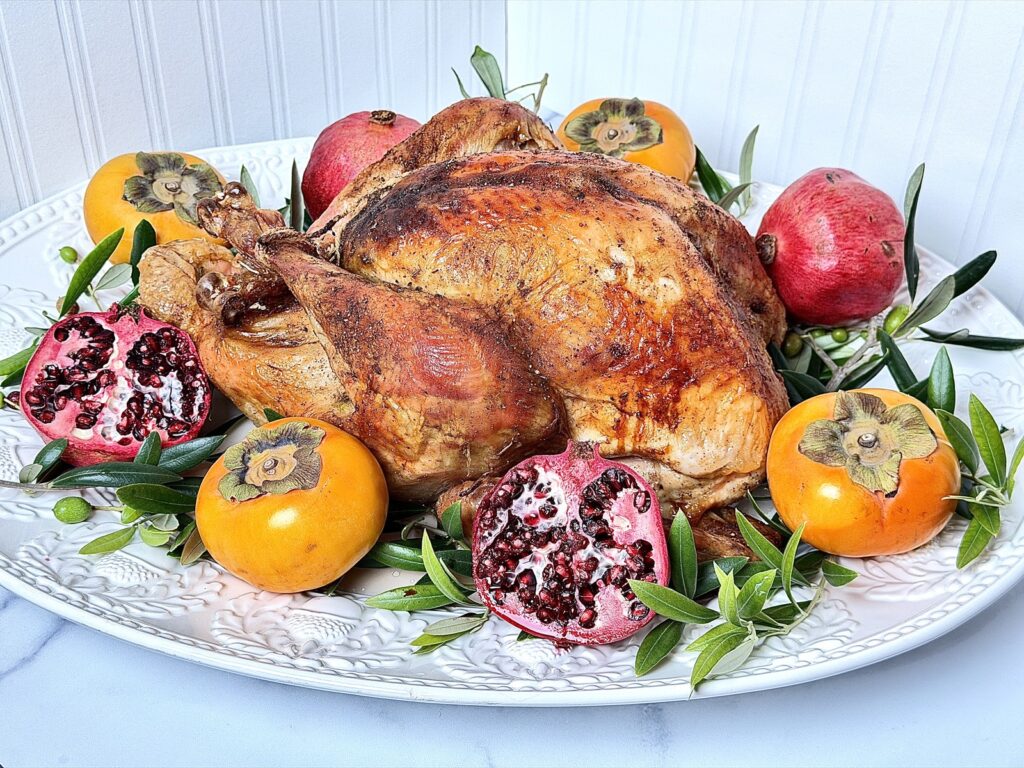 Image of the perfect turkey on a white serving platter with acorns, olive branches, pomegranates, and persimmons on a marble counter