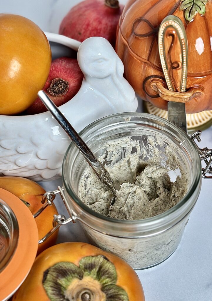 Image of savory poultry seasoning, compound butter in a glass Kilner clip top jar surrounded by persimmons, pomegranate, pottery, barn, porcelain turkey, gravy, boat, and a porcelain pumpkin