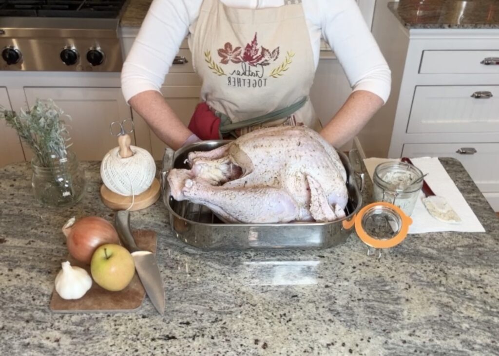 Image of a woman in an apron standing behind a counter that contains the ingredients to make the perfect turkey