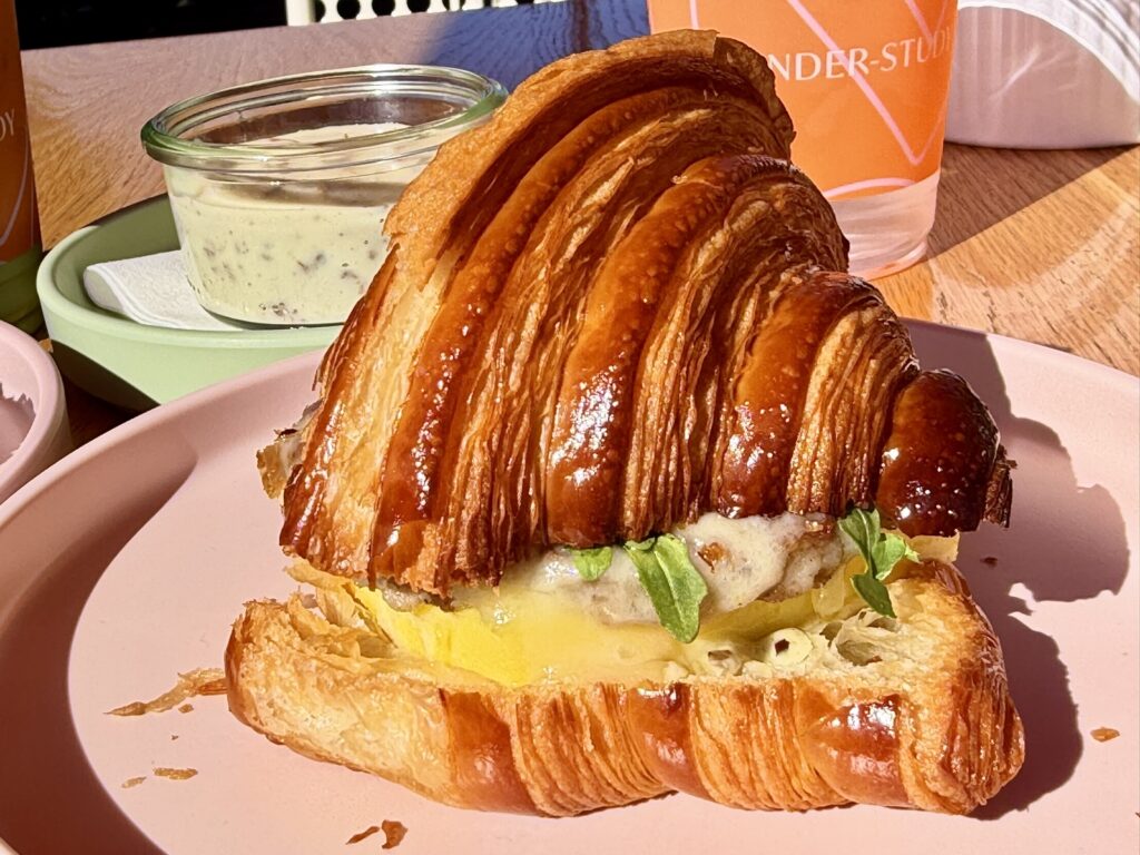 A picture of the breakfast sandwich from Under-Study in Saint Helena, which is on a house-made croissant with egg, sausage, melted cheese, and Padron pepper aïoli.