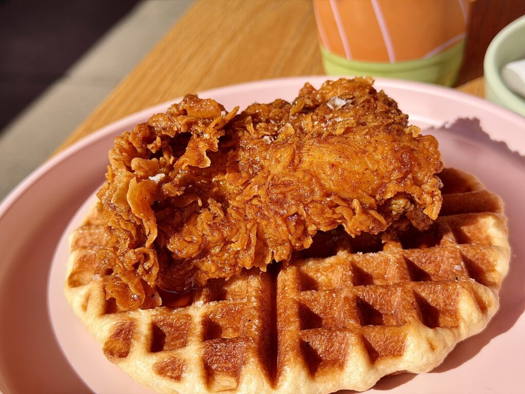 A picture of understudies, hot chicken N croffle on a pink plate with a green matcha latte in the background.