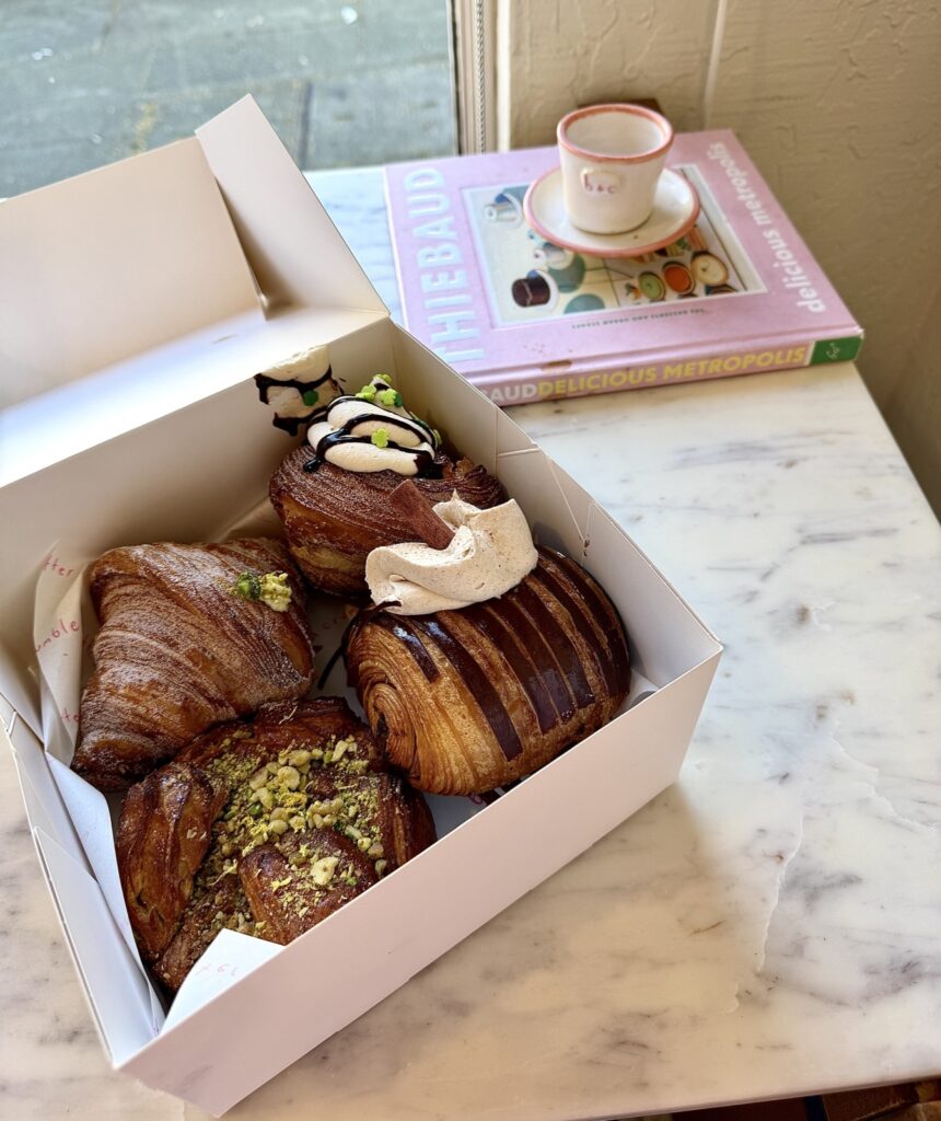 A picture of four sweet pastries from butter and crumble on a marble table with a butter and crumble espresso cup behind the box