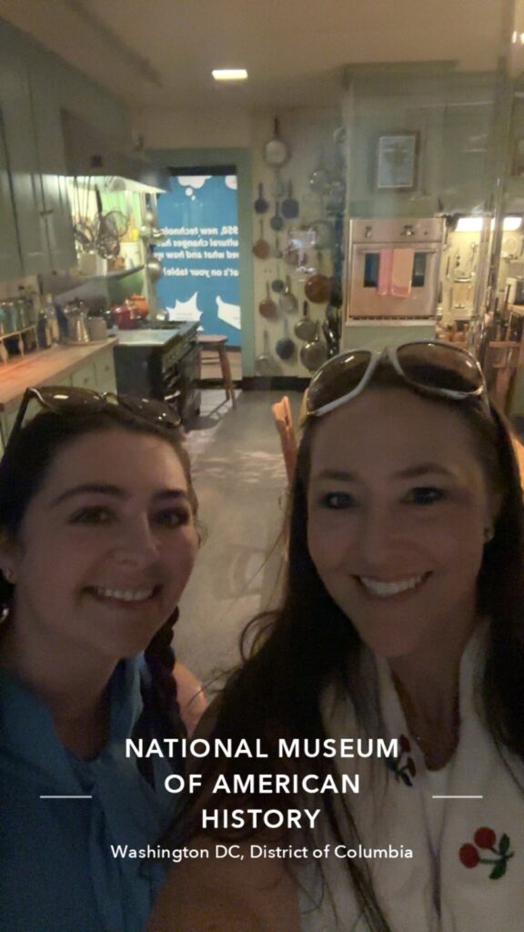 A picture of Julia Child at the National Museum of American History in Washington DC, two women taking a selfie in front of Julia's kitchen
