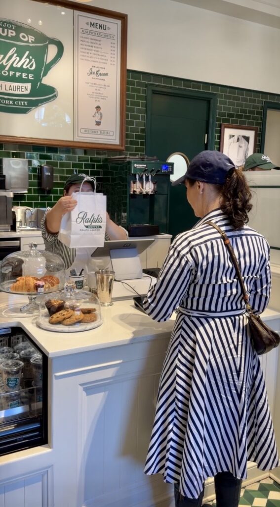 A picture of a woman wearing a blue and white striped Ralph Lauren dress and a blue Ralph Lauren Polo hat checking out at the Ralph's coffee counter