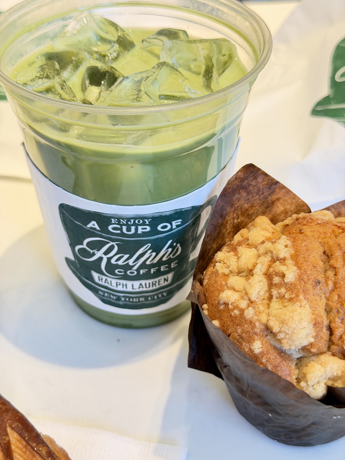 A picture of an iced latte in a Ralph, coffee, coffee collar, and a blueberry muffin