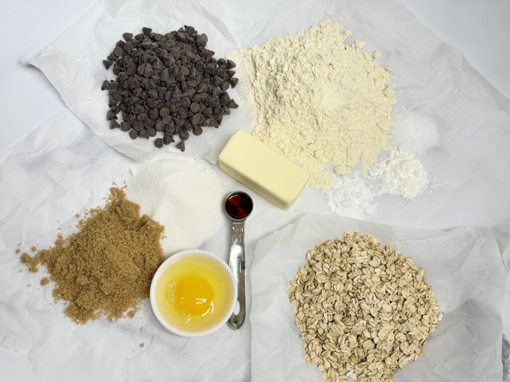 A picture of Einhorn, all purpose, flour, salt, cornstarch, baking soda, butter, white sugar, brown sugar, one egg, vanilla, chocolate chips, and oats. This picture is all of the ingredients to make einkorn chocolate chip oatmeal cookies