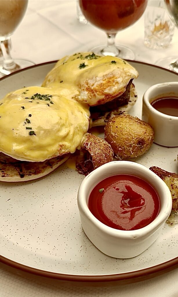 Brunch at Baltaire: a picture of eggs, Benedict with steak and roasted potatoes on a white plate with a brown rib and a stone ramekin with ketchup