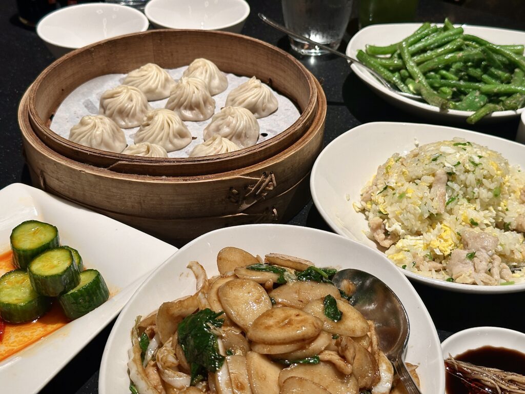 A picture of a Din Tai Fung dinner with rice, cakes, soup dumplings, fried rice, garlic, green beans, and cucumber salad