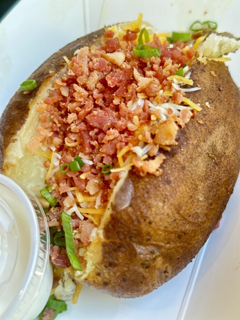 A picture of a loaded baked potato from Troubadour Tavern at Disneyland. This is the Troubadour Baked Potato: butter, sour cream cheese, bacon, and green onions.