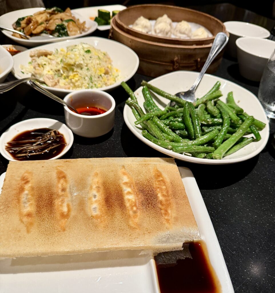A picture of a table full of food from Din Tai Fung. Potstickers, garlic green beans, fried rice, soup, dumplings, and rice cakes.