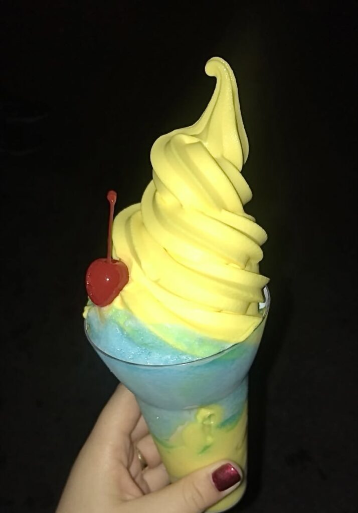 A picture of the Pixar Pier Frosty Parfait from Adorable Snowman Frosted Treats. Yellow and blue drink with a red cherry.