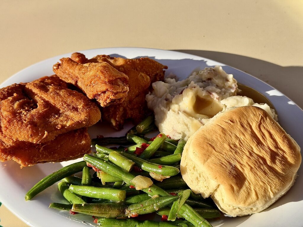 A picture of the fried chicken dinner from Plaza Inn in Disneyland, California. The fried chicken dish includes three pieces of fried chicken, green beans, mashed potatoes and gravy and a biscuit.