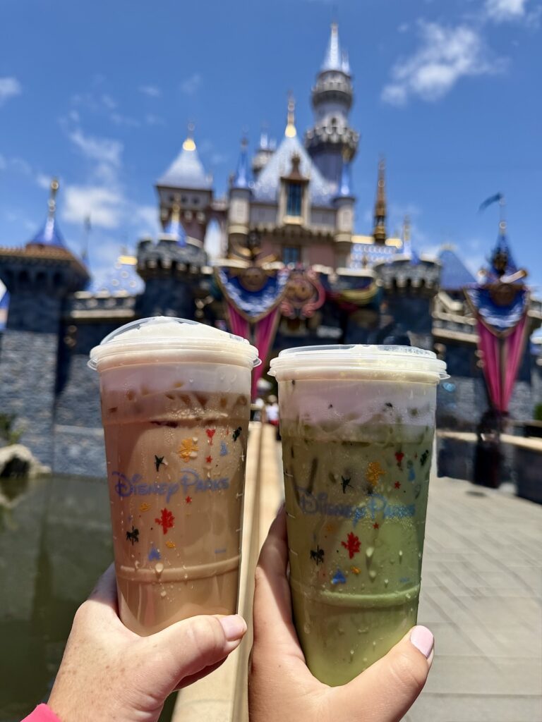A picture of an iced Matcha and an iced latte in Disney Starbucks cups from Starbucks in Disneyland taken in front of Sleeping Beauty's Castle.